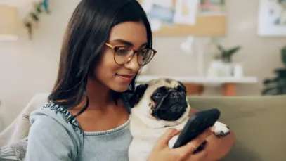 Tutora com cachorro da raça pug no colo enquanto faz compras pelo celular